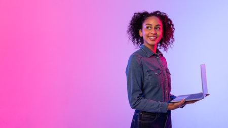 Smiling black woman holding laptop on vivid gradient backdrop, copy spaceの写真素材