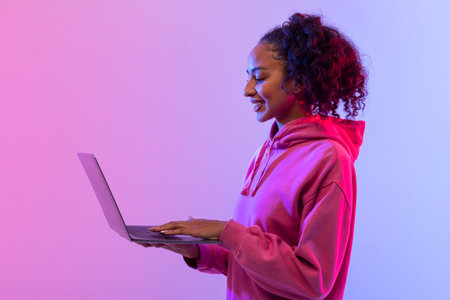 Joyful black woman with laptop on colorful neon backgroundの写真素材
