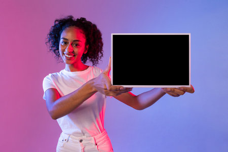 Cheerful black lady holding tablet with black screen, gradient backgroundの写真素材
