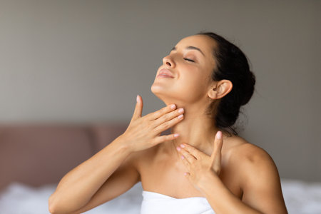 Happy caucasian lady applies moisturizer massaging neck at bedroomの写真素材