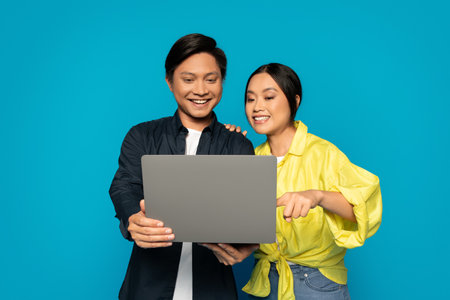 Enthusiastic Asian couple collaboratively working on a laptop with attentive and joyful expressionsの写真素材