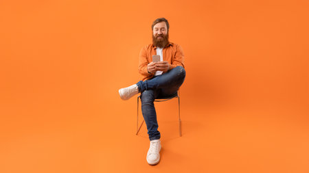 Redhaired man smiles while texting on his smartphone in studio