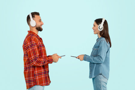 Couple With Headphones Holding Smartphones Listening Music Against Blue Background