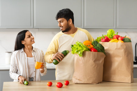 Happy Indian Couple Unpacking Bag With Groceries In Kitchenの写真素材