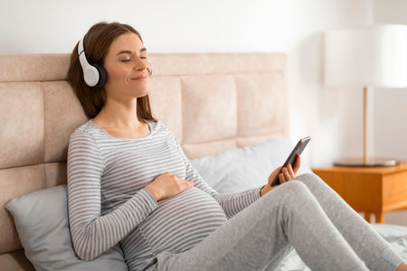Expecting mother relaxing with headphones and phoneの写真素材