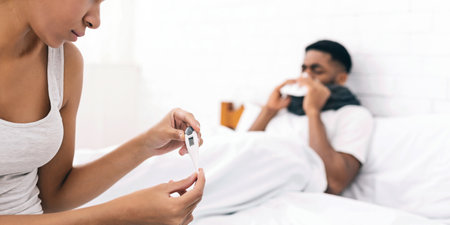Woman taking care of sick man with fever lying in bed