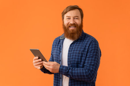 Cheerful redhaired bearded man in casual holding digital tablet, studioの写真素材