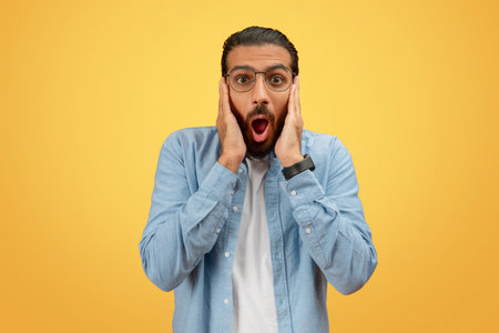 Shocked man with hands on cheeks on yellowの写真素材