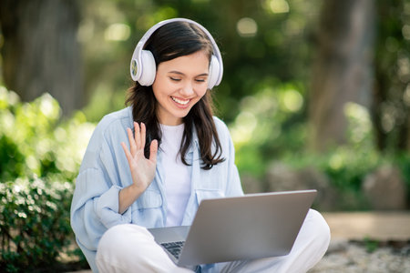 Engaging young woman with headphones, waving at her laptop screenの写真素材