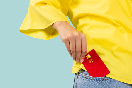 Close up photo shot of female hand putting credit bank card in jeans front pocket isolated on blueの写真素材