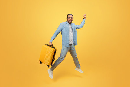 Man jumping with suitcase on yellow backgroundの写真素材