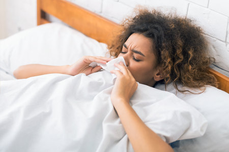 Young sick woman blowing her nose in bedの写真素材