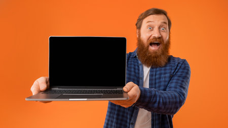 Bearded redhaired man holding laptop showing screen with excitement, studioの写真素材