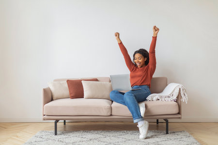 Joyful Black Woman Celebrating Success at Home During Daytimeの写真素材