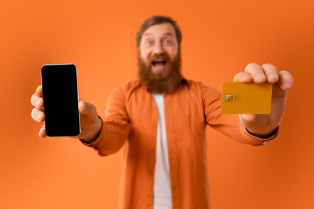 Cheerful bearded man showing cellphone screen and credit card, studioの写真素材
