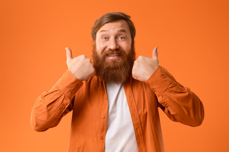 Cheerful Man With Red Beard Gesturing Thumbs Ups, Orange Studioの写真素材