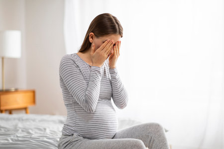 Sad pregnant woman sitting on bed covering faceの写真素材