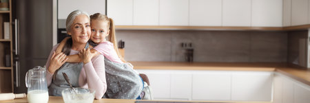 Smiling little girl hugs old woman in kitchen interiorの写真素材