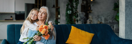 Happy small girl hugs caucasian old grandmother, gives flowers
