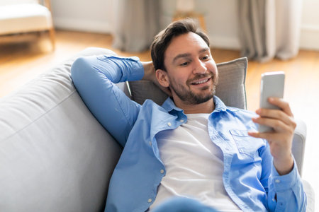 Positive Man Sitting on Couch Looking at Phoneの写真素材