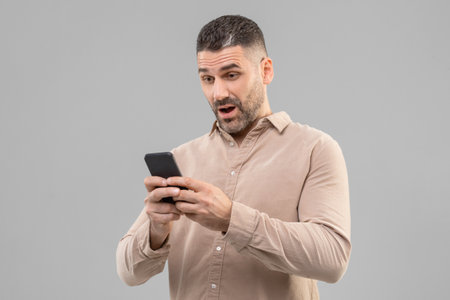 Surprised Mature Man Holding Cell Phone, Grey Backgroundの写真素材