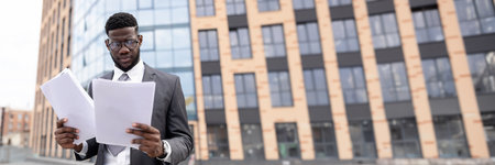 Young black man in suit checking reports outdoorsの写真素材