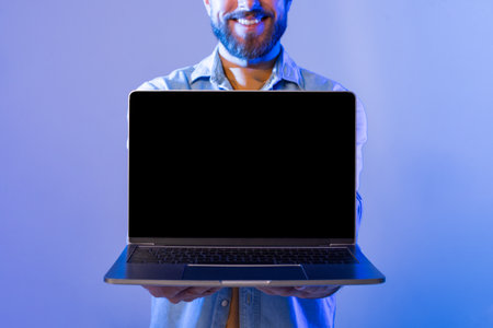 Smiling Bearded Man Holding Laptop Screen Forward in Blue Backgroundの写真素材