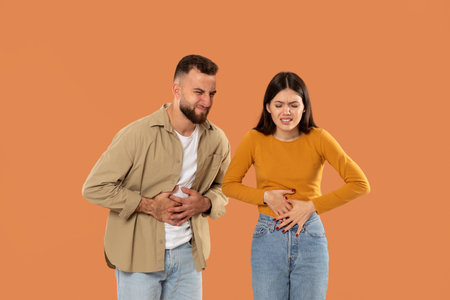 Young Couple Experiences Stomach Pain Against Orange Backgroundの写真素材
