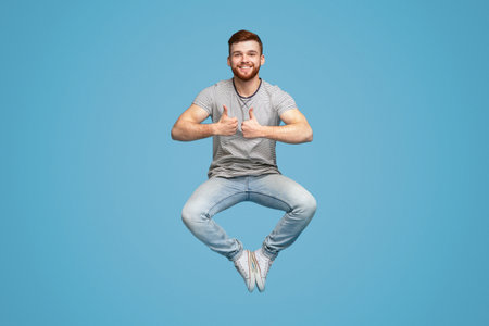 Joyful man jumping up in air, demonstrating thumbs up gesture