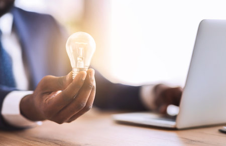 Businessman holding illuminated light bulb, sitting in officeの写真素材