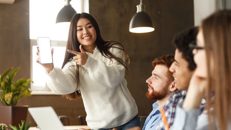 Asian girl showing cellphone to classmates, pointing at blank screen