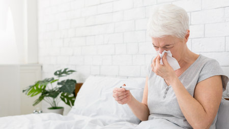 Sick senior woman measuring body temperature in bed