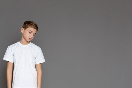 Sad teen boy looking down on grey backgroundの写真素材