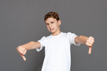 Young boy showing thumbs down gesture isolated on greyの写真素材