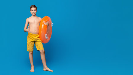 Teen Boy Holding Orange Inflatable Ring Against Bright Blue Backgroundの写真素材