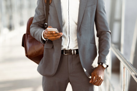 Businessman using phone, standing with luggage in airport, cropped