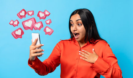 Amazed Indian woman texting on smartphone expressing wow, blue background