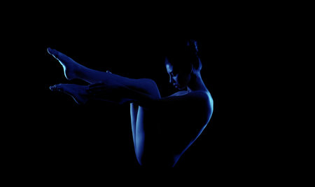 Woman Posing in Blue Light With Legs Extended Against Black