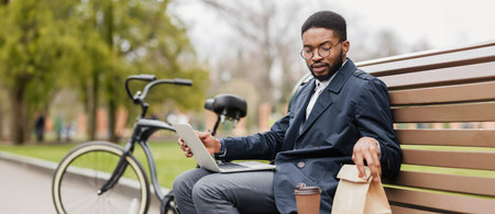 Professional man using laptop, bike nearby in parkの写真素材