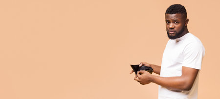 African American Man Showing Empty Wallet Against Beige Backgroundの写真素材