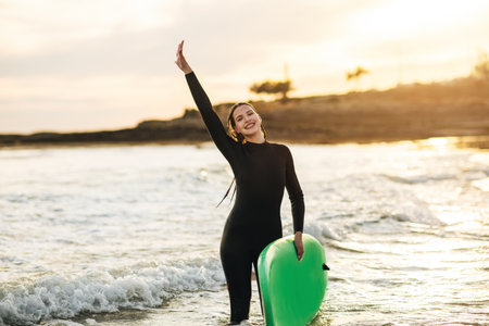 Woman in Wetsuit Holding Green Surfboard in Ocean at Sunsetの写真素材