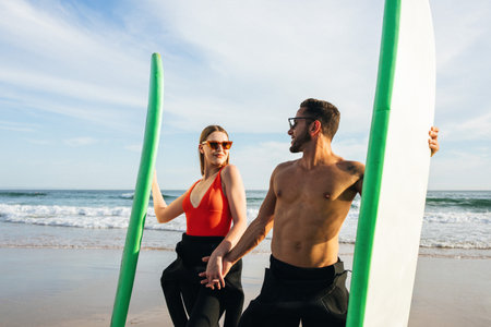 Couple Holding Surfboards on Sandy Beach With Ocean Waves