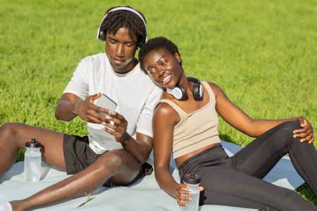 Couple Relaxing on Blanket in Park Using Smartphonesの写真素材