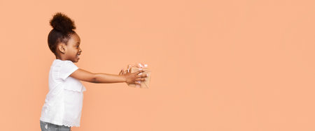 Happy Little Girl Holding a Gift Against Peach Studio Backgroundの写真素材