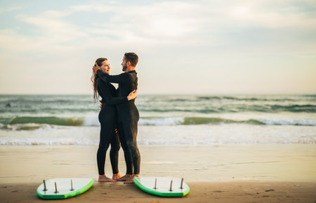 Couple Embracing on Sandy Beach With Surfboards at Sunsetの写真素材