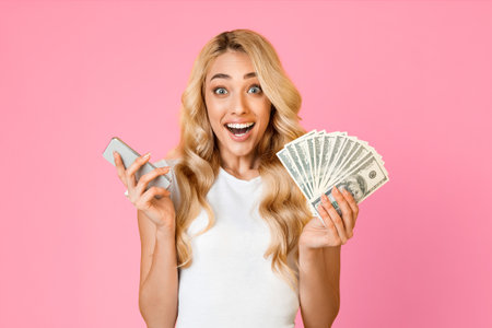 Excited Woman Holding Cash and Smartphone Against Pink Background