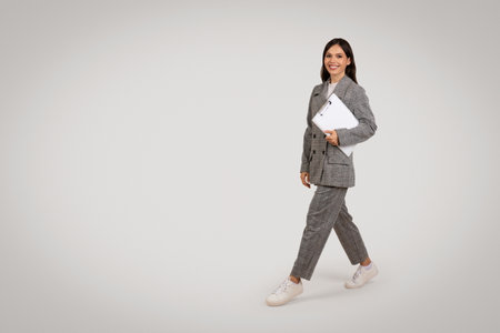Walking businesswoman in plaid suit with laptop, on the goの写真素材