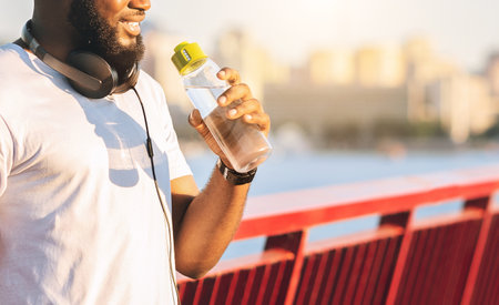 Young black guy drinking water, staying on the bridgeの写真素材