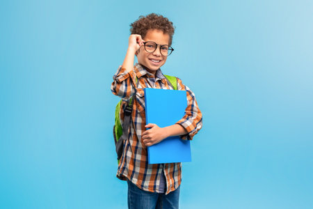 Smiling student in plaid, adjusting glasses, blue folder