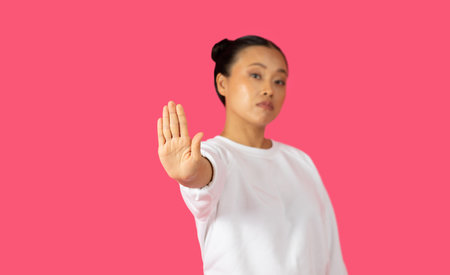 Young Woman Holding Up Hand In Stop Gesture Against Pinkの写真素材